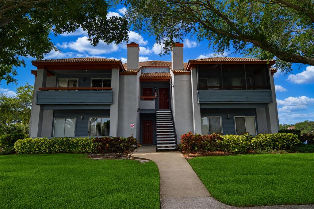 A two-story apartment building with a central staircase, balconies, and a landscaped lawn — 10263 GANDY BOULEVARD N UNIT 405, ST PETERSBURG, FL