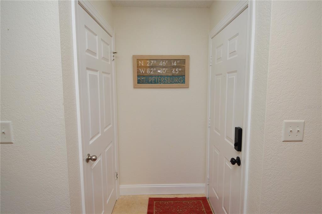 A hallway features two white doors, a red rug, and a St. Petersburg coordinates sign — 10263 GANDY BOULEVARD N UNIT 405, ST PETERSBURG, FL