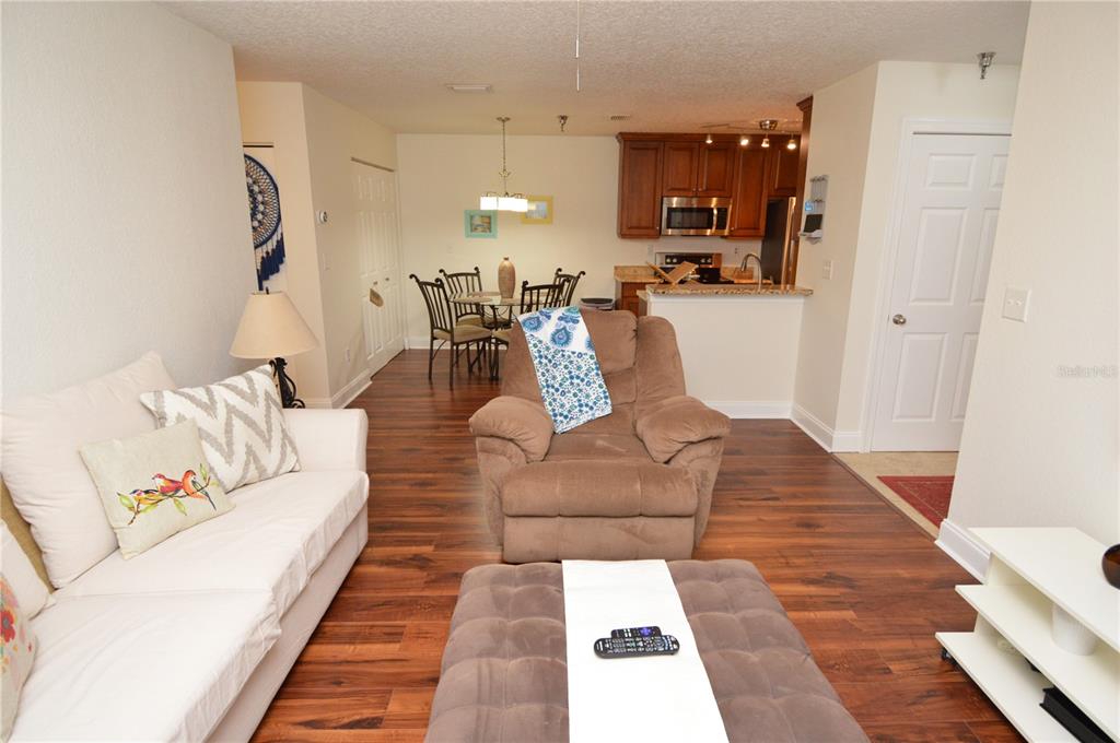 A living room with wood-look flooring, a white sofa, a brown recliner, and an open kitchen — 10263 GANDY BOULEVARD N UNIT 405, ST PETERSBURG, FL