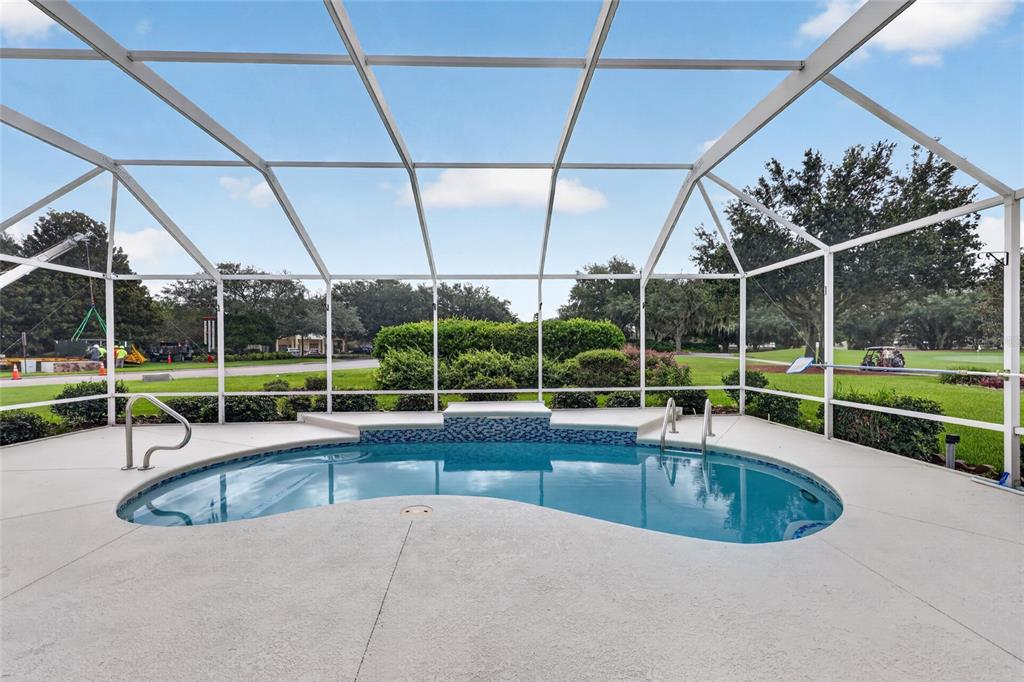 A screened-in swimming pool with a raised tiled spillway sits on a concrete patio — 745 DOWDING WAY, THE VILLAGES, FL