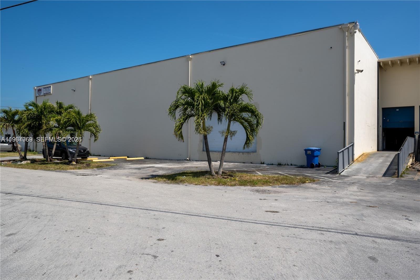 A beige industrial warehouse building features palm trees, a loading ramp, and a parking area — 11441 SW 208th Dr, Miami FL 33189, MIAMI, FL