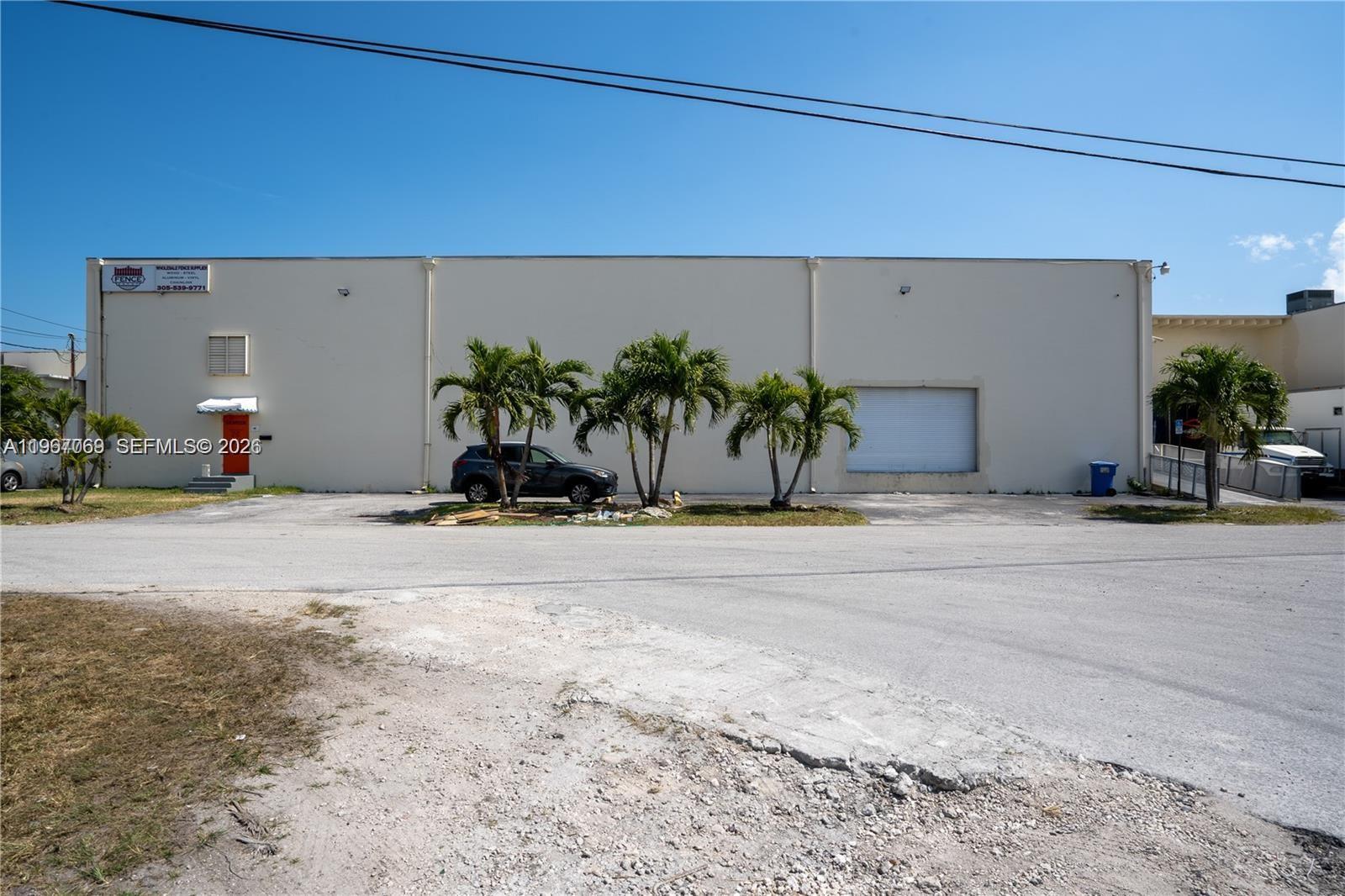 A beige industrial warehouse building features a roll-up door, a small entrance, and palm trees — 11441 SW 208th Dr, Miami FL 33189, MIAMI, FL