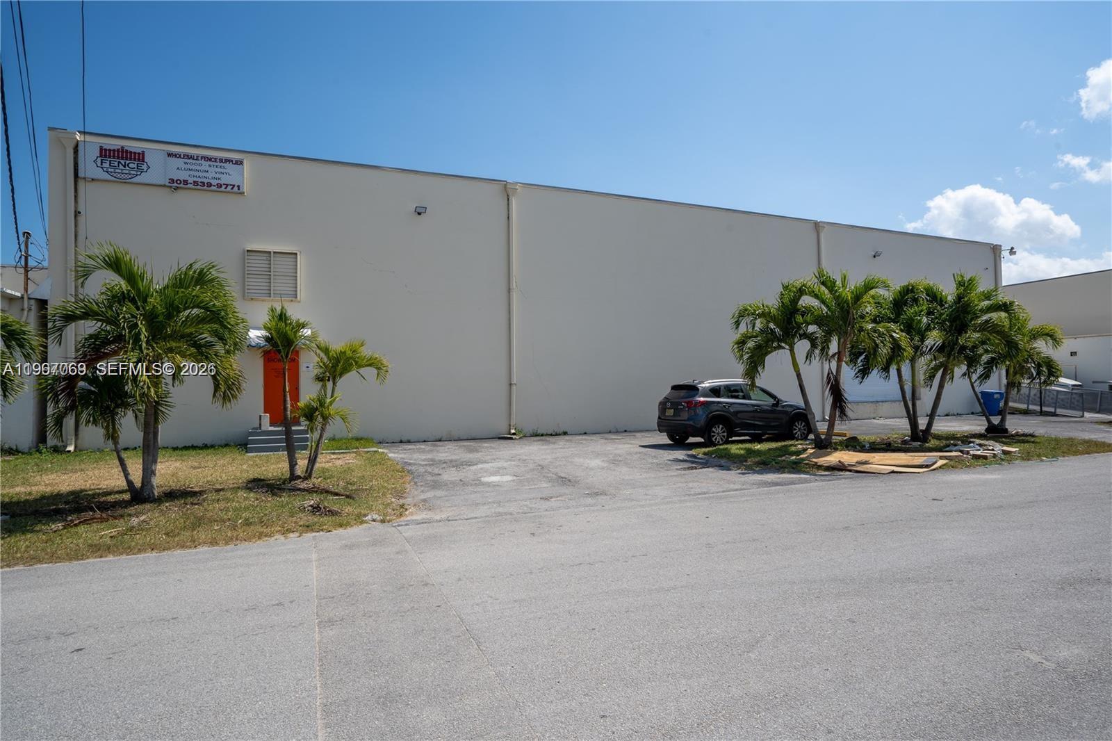 A beige industrial warehouse building features a bright orange door and several palm trees — 11441 SW 208th Dr, Miami FL 33189, MIAMI, FL