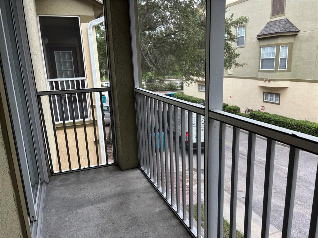 A screened-in balcony with concrete flooring and metal railings overlooks a parking area — 2424 GRAND CENTRAL PARKWAY UNIT 17, ORLANDO, FL