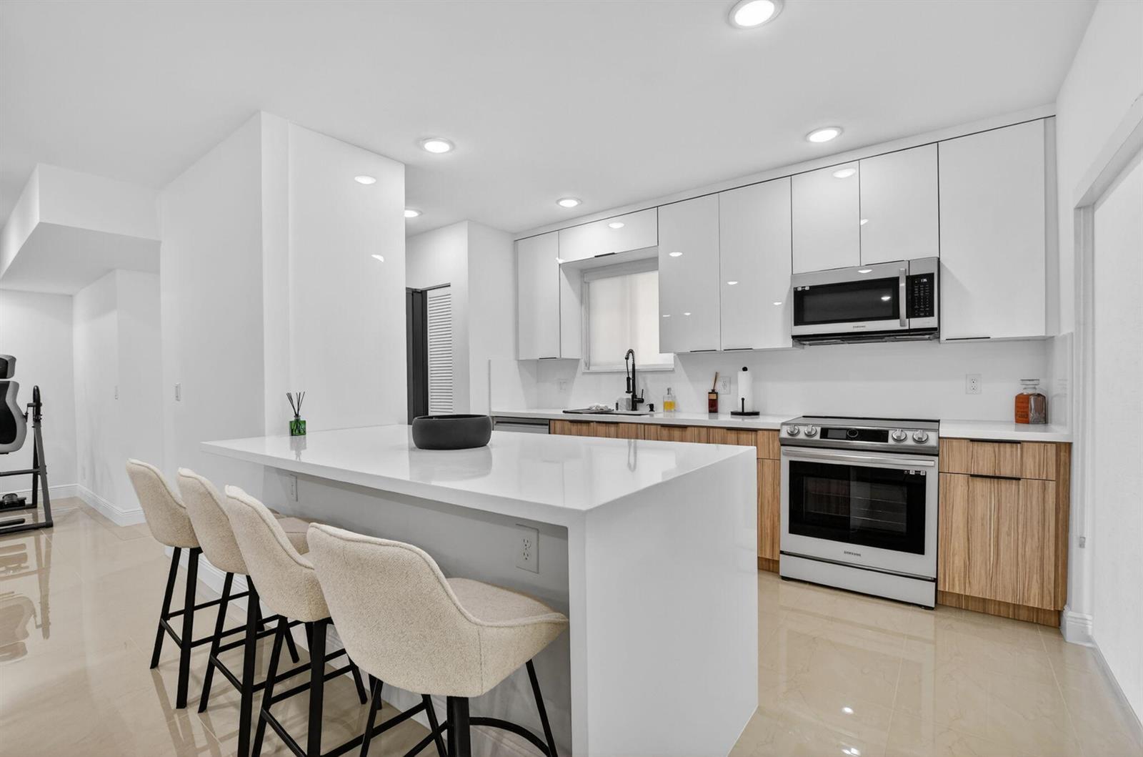 A modern kitchen features white upper cabinets, wood-grain lower cabinets, a white island, and barstools — 6335 Longboat Lane W # E104, Boca Raton FL 33433, BOCA RATON, FL