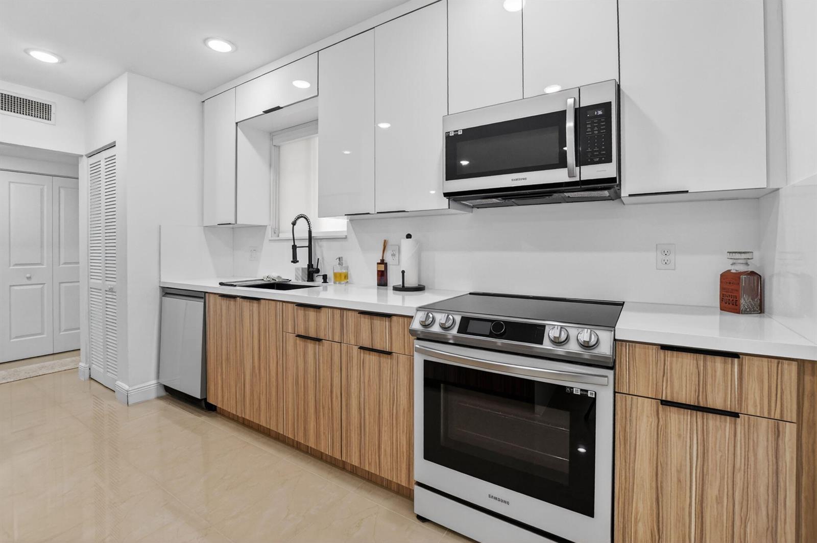 A modern kitchen features white upper cabinets, wood-grain lower cabinets, and stainless steel appliances — 6335 Longboat Lane W # E104, Boca Raton FL 33433, BOCA RATON, FL