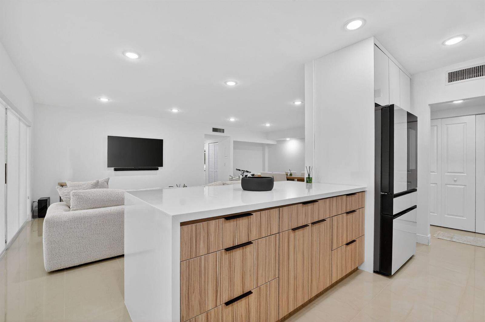 A modern kitchen island with wood-grain cabinets and a white countertop faces a living area — 6335 Longboat Lane W # E104, Boca Raton FL 33433, BOCA RATON, FL