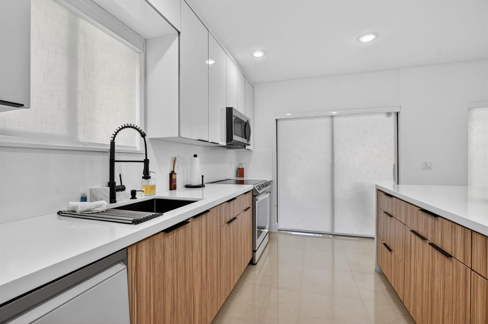 A modern kitchen features white upper cabinets, wood-grain lower cabinets, white countertops, and black fixtures — 6335 Longboat Lane W # E104, Boca Raton FL 33433, BOCA RATON, FL