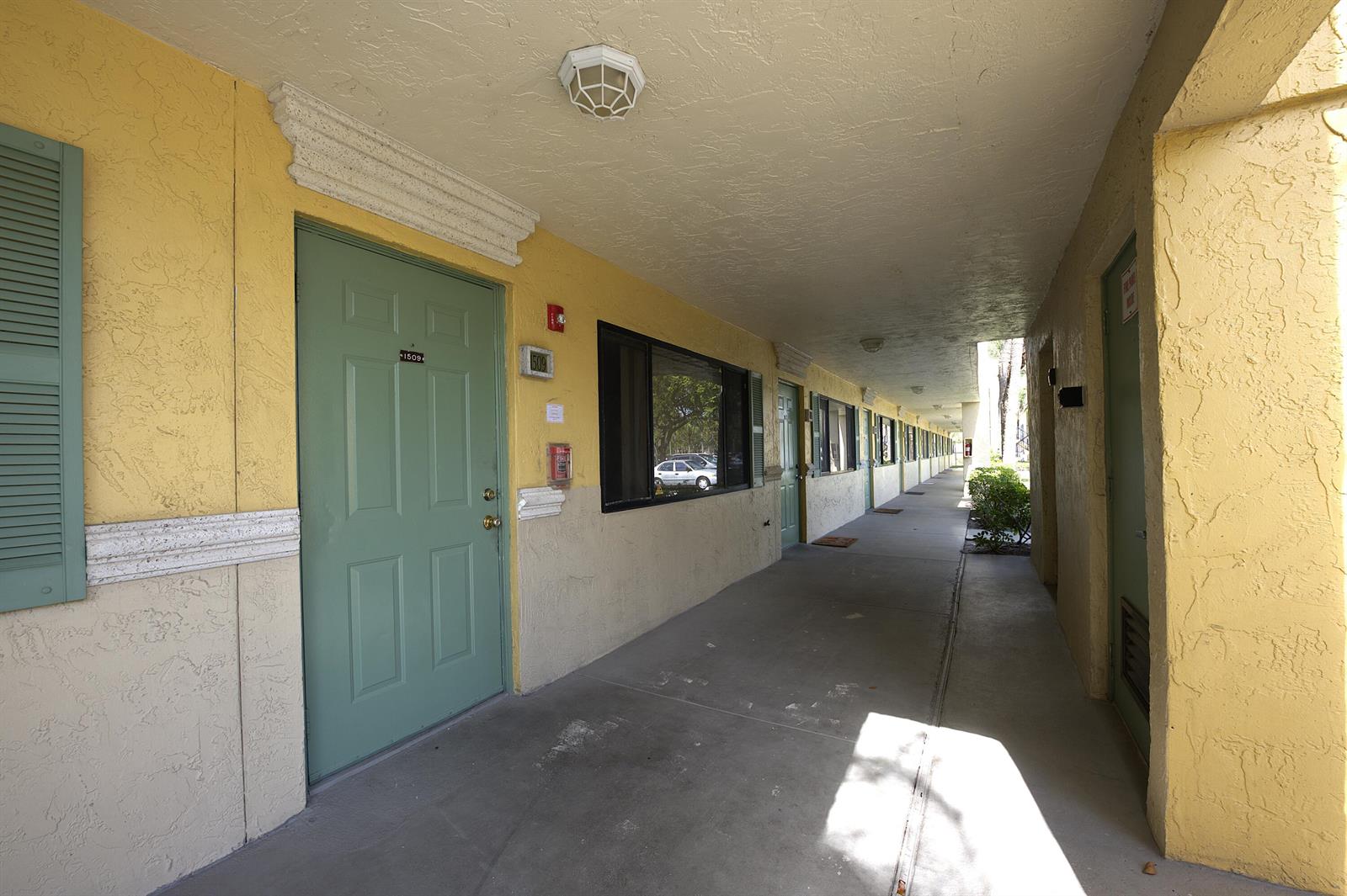 An exterior walkway of a multi-story building features yellow stucco walls and green doors — 1509 Meadows Circle W, Boynton Beach FL 33436, BOYNTON BEACH, FL