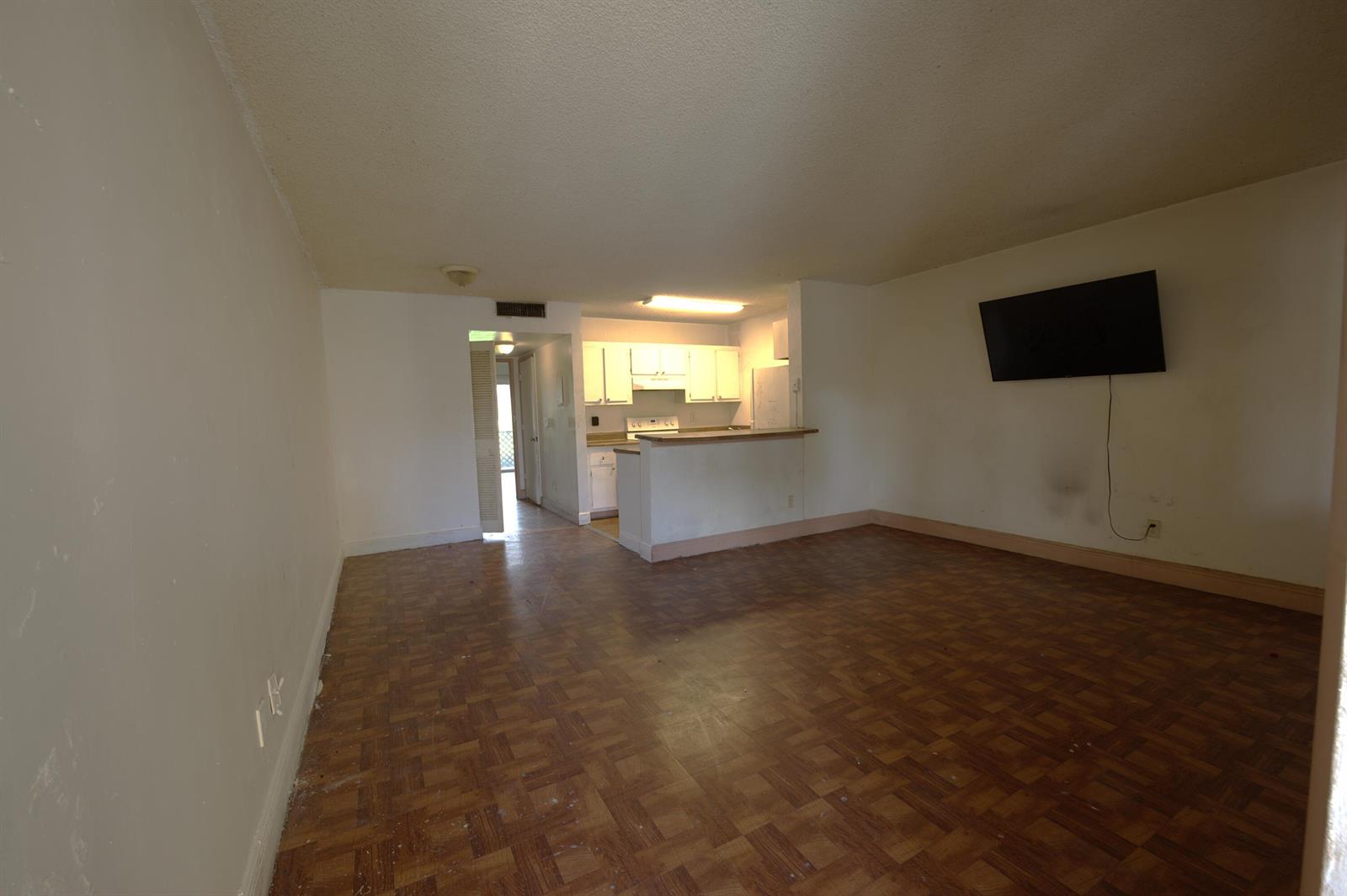 An empty living room with parquet flooring, a wall-mounted television, and an open kitchen beyond — 1509 Meadows Circle W, Boynton Beach FL 33436, BOYNTON BEACH, FL