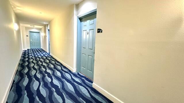 A hotel hallway features blue patterned carpet, light-colored walls, and several teal doors — 100 NE 6th Street # 709, Boynton Beach FL 33435, BOYNTON BEACH, FL