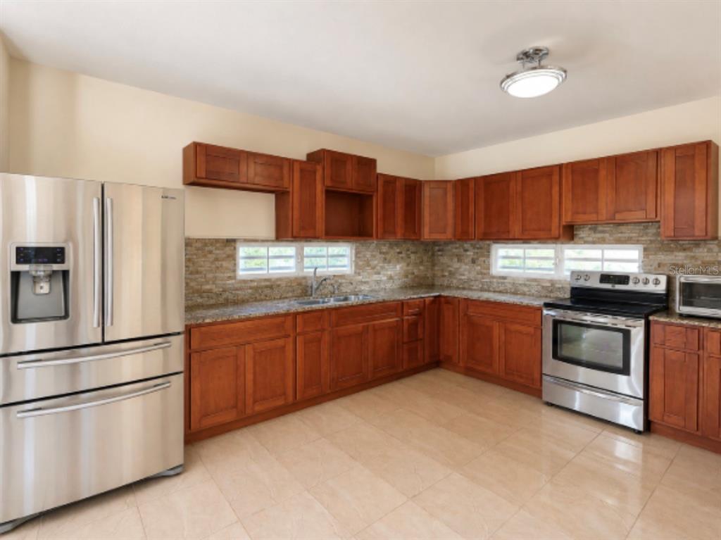 A kitchen featuring wood cabinets, stainless steel appliances, granite countertops, and a stone backsplash — 22 MANSIONES DE TERRALINDA, LUQUILLO, PR