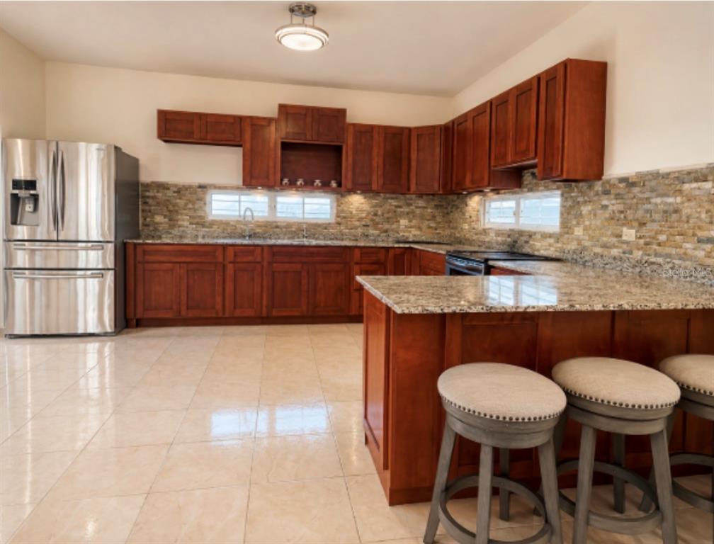 A kitchen features wood cabinets, granite countertops, a stone backsplash, and stainless steel appliances — 22 MANSIONES DE TERRALINDA, LUQUILLO, PR