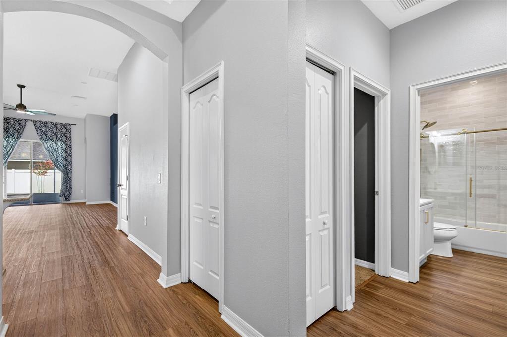 A hallway with wood-look flooring leads past several white doors toward a bright living area — 12005 RAMBLING STREAM DRIVE, RIVERVIEW, FL