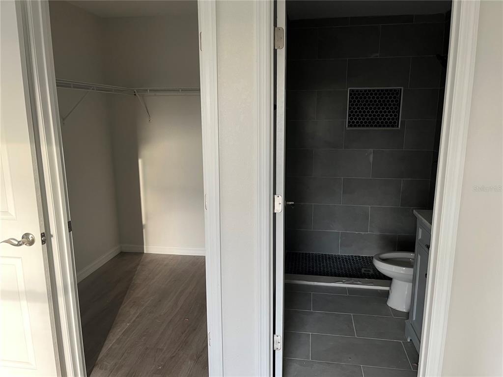 A walk-in closet with shelving sits next to a bathroom featuring gray tiled walls — 6917 SAN BENITO DRIVE, SEBRING, FL