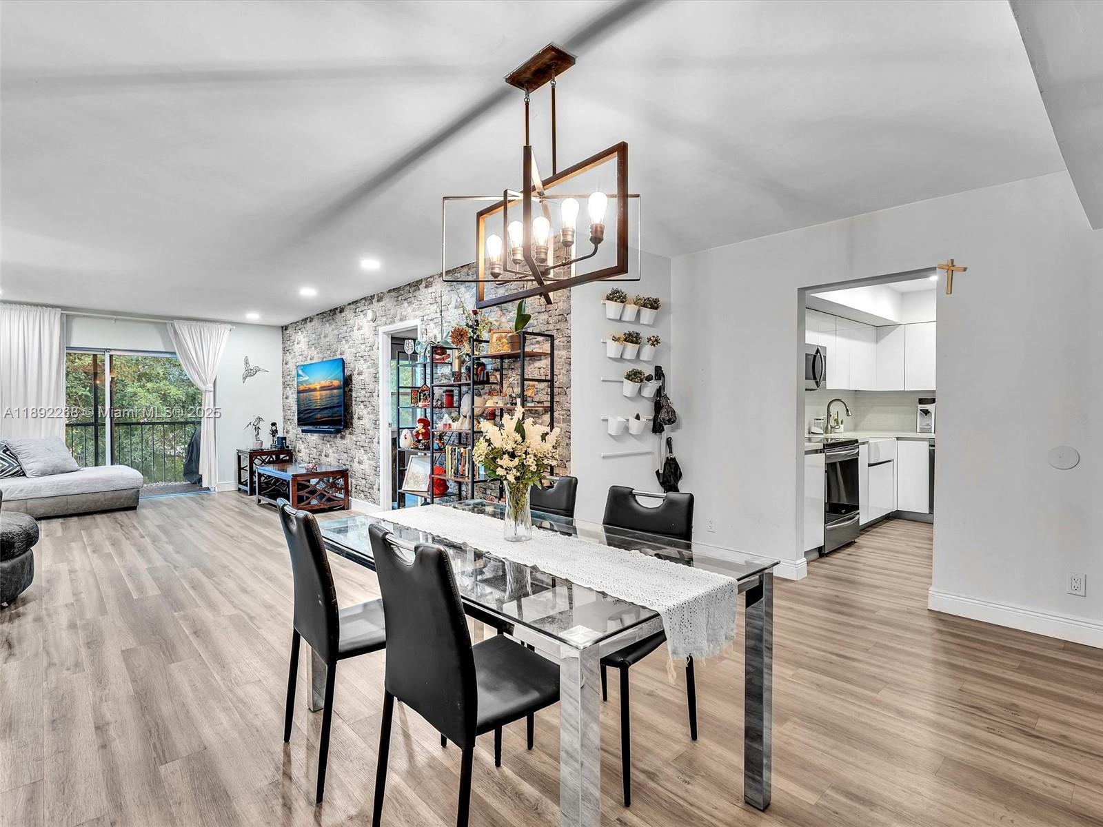 A dining area with a glass table and chandelier sits before a stone accent wall — 6061 N Falls Cir Dr # 407, Lauderhill FL 33319, LAUDERHILL, FL
