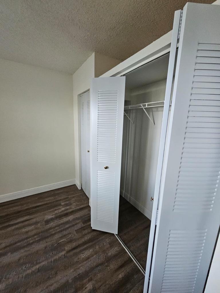 A room with wood-look flooring and two white louvered-door closets with wire shelving inside — 18335 NW 68 Avenue # 104a, Hialeah FL 33015, HIALEAH, FL