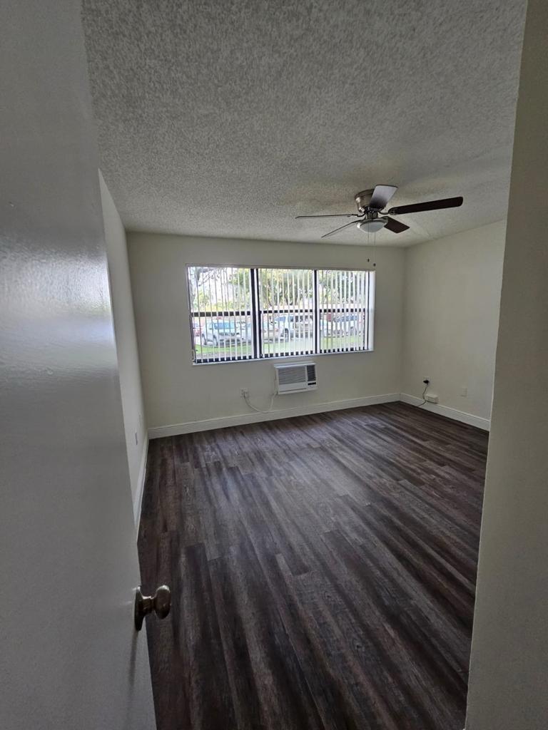 An empty bedroom with dark wood-look flooring, a ceiling fan, and a window air conditioner — 18335 NW 68 Avenue # 104a, Hialeah FL 33015, HIALEAH, FL