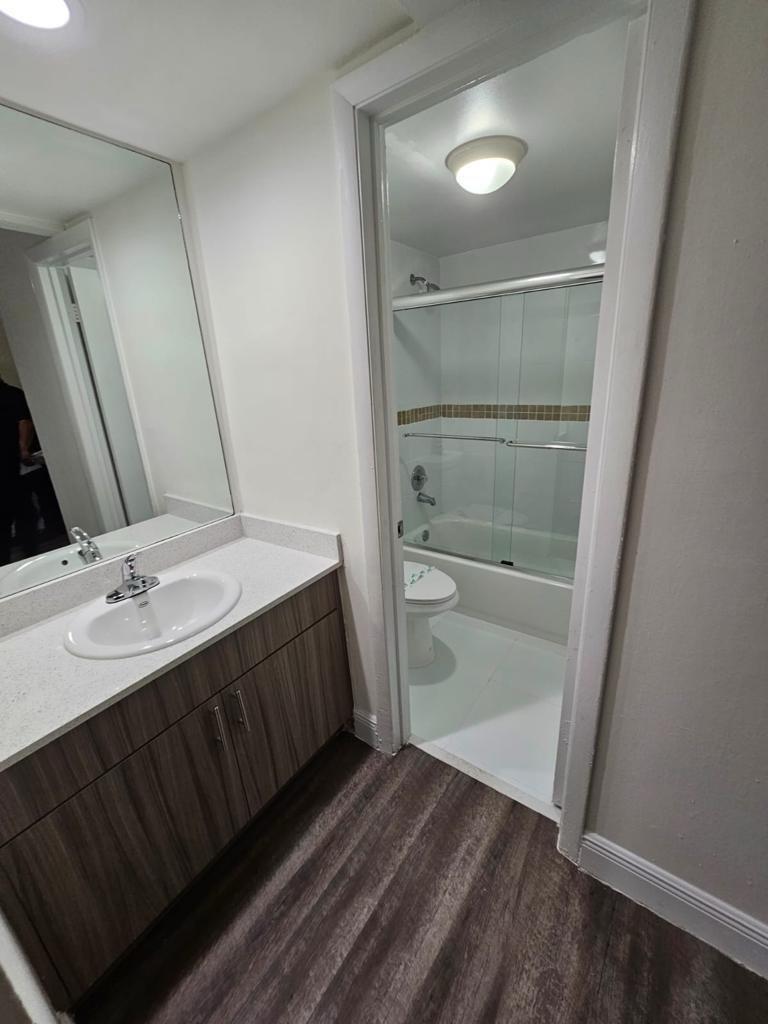 A bathroom features a wood-grain vanity, white countertop, large mirror, and a separate tub-shower area — 18335 NW 68 Avenue # 104a, Hialeah FL 33015, HIALEAH, FL