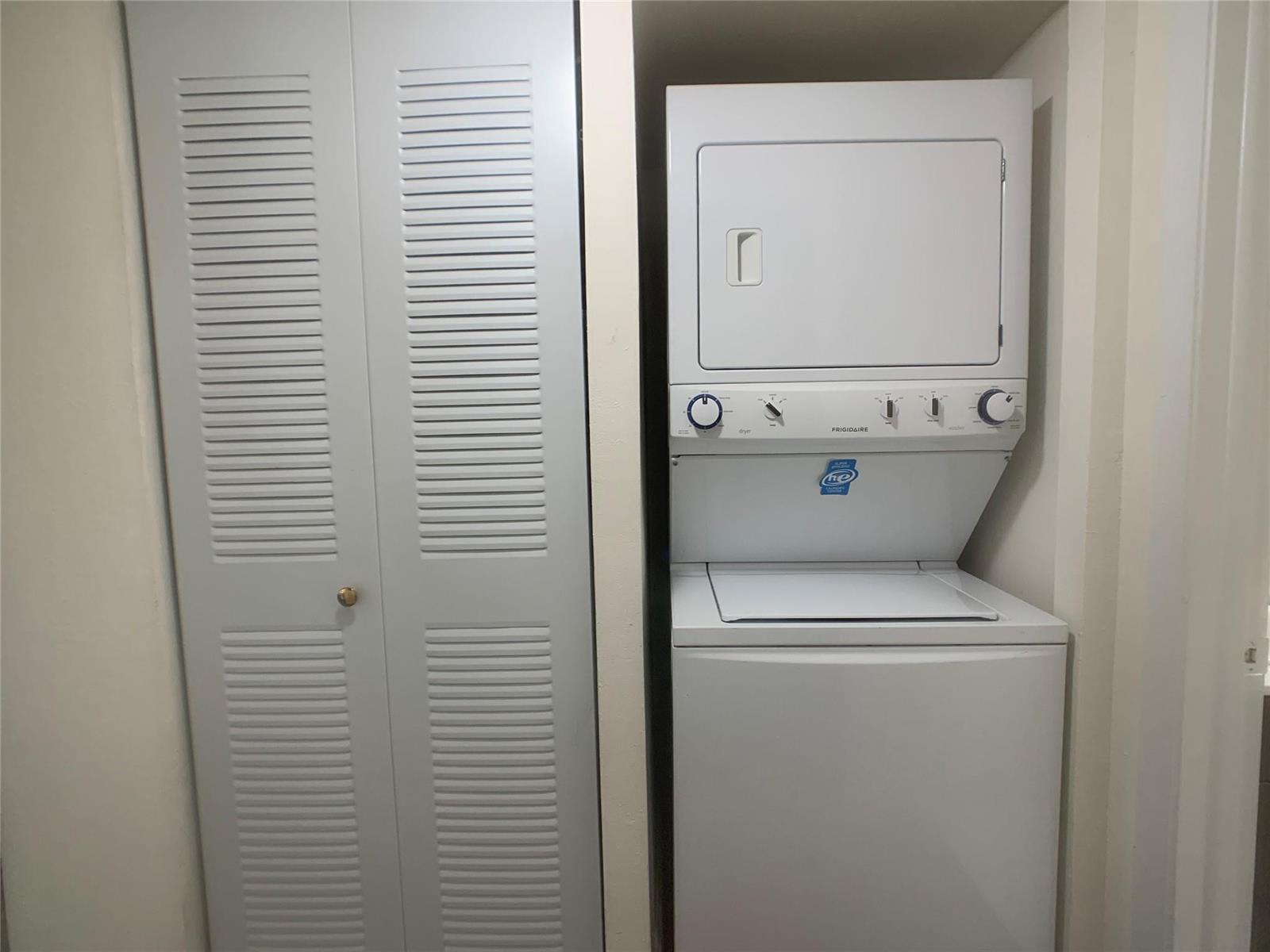 A white stacked Frigidaire washer and dryer unit sits next to a louvered closet door — 18335 NW 68 Avenue # 104a, Hialeah FL 33015, HIALEAH, FL