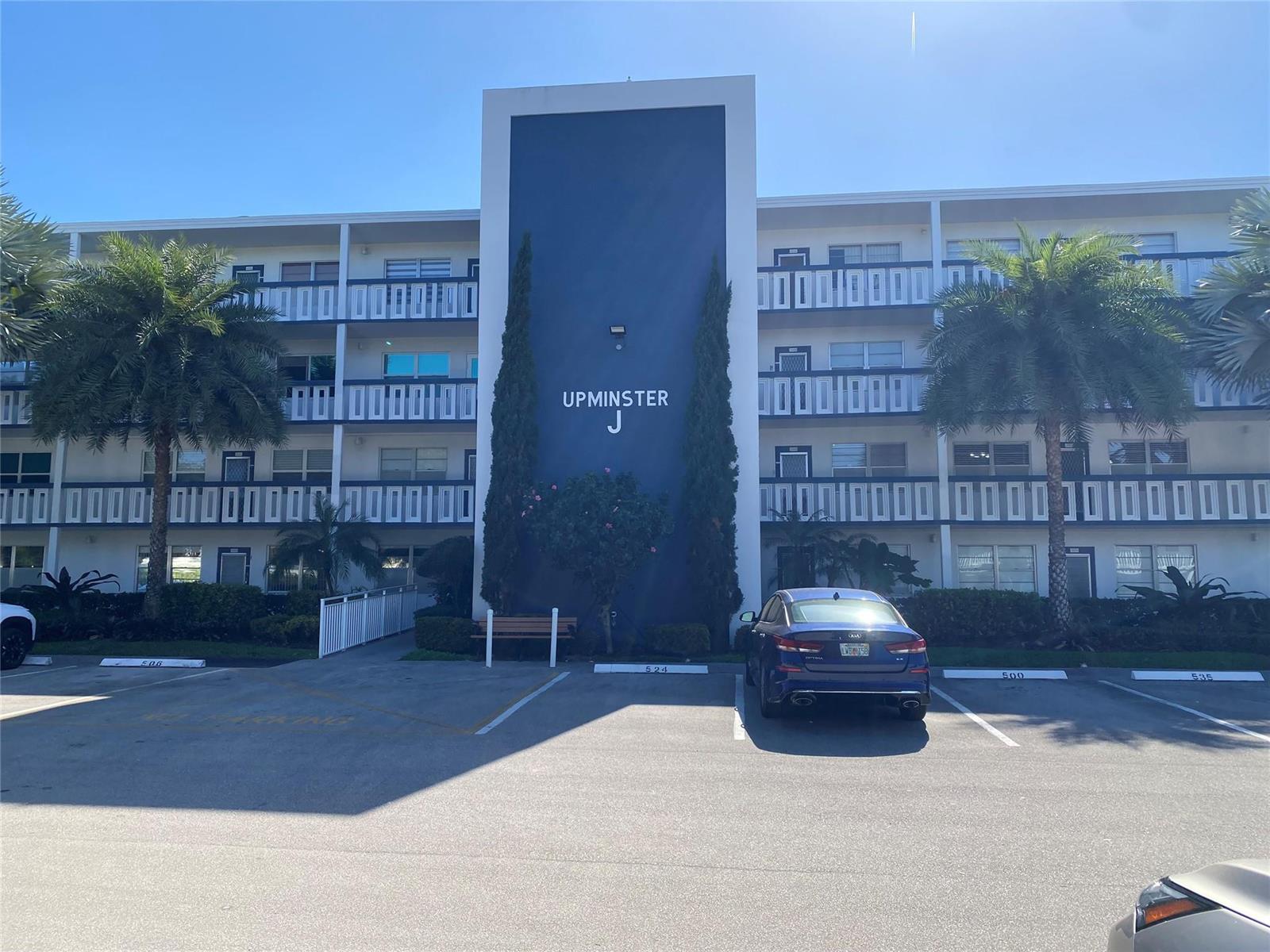 A three-story apartment building with a blue central facade labeled Upminster J and parking — 4011 Upminster J # 4011, Deerfield Beach FL 33442, DEERFIELD BEACH, FL