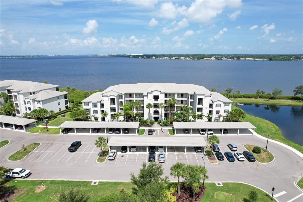 An aerial view shows a multi-story apartment building with covered parking spaces and a lake — 1030 TIDEWATER SHORES LOOP UNIT 104, BRADENTON, FL