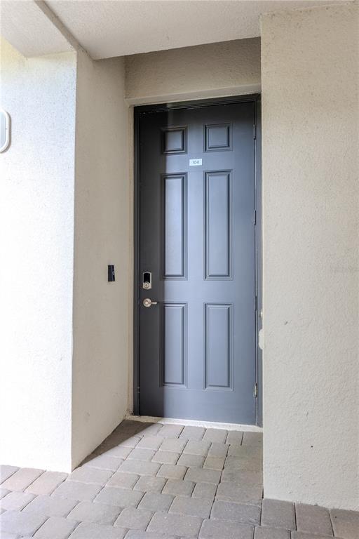 A dark gray six-panel door with a smart lock is set in a stucco entryway — 1030 TIDEWATER SHORES LOOP UNIT 104, BRADENTON, FL