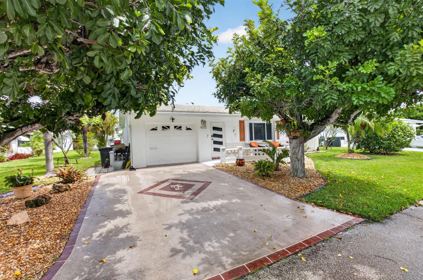 A white single-story house with a garage and a paved driveway sits under large trees — 1803 SW 22nd Way, Boynton Beach FL 33426, BOYNTON BEACH, FL