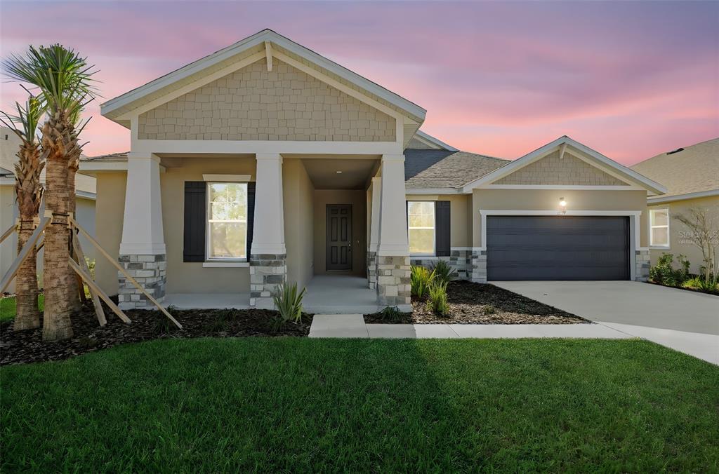A single-story suburban house features a tan exterior, stone accents, a covered porch, and garage — 17374 CRISP APPLE LANE, LAND O LAKES, FL