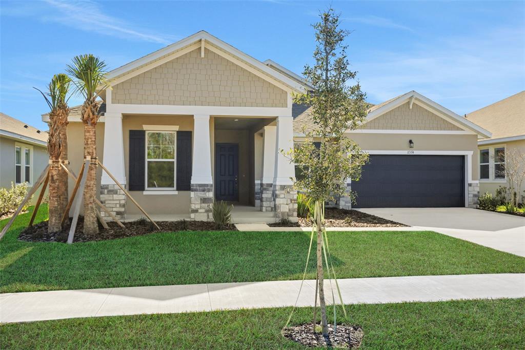 A single-story house with a tan exterior, stone accents, a dark garage door, and landscaping — 17374 CRISP APPLE LANE, LAND O LAKES, FL