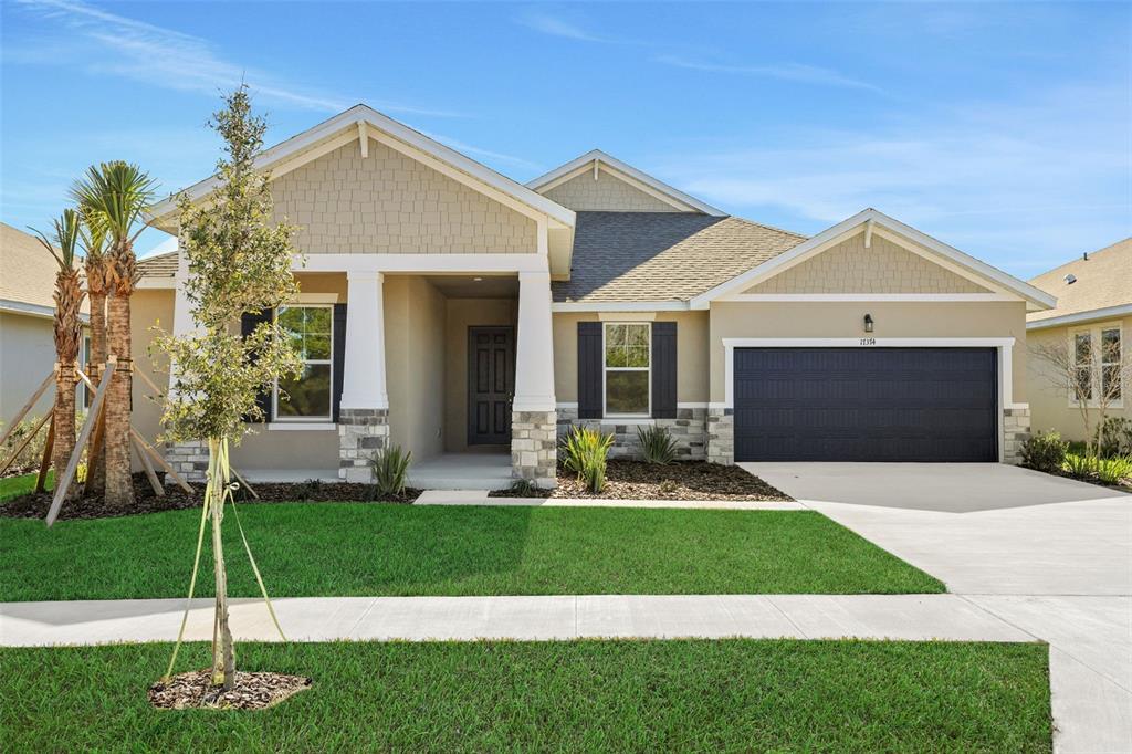 A single-story suburban house with a tan exterior, stone accents, and a dark garage door — 17374 CRISP APPLE LANE, LAND O LAKES, FL