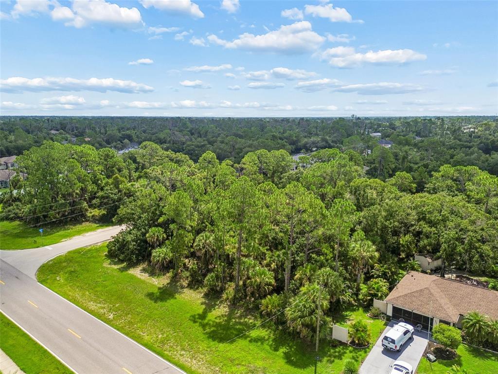 An aerial view shows a wooded vacant lot situated between a paved road and a house — 14 S CHAMBERLAIN BOULEVARD, NORTH PORT, FL