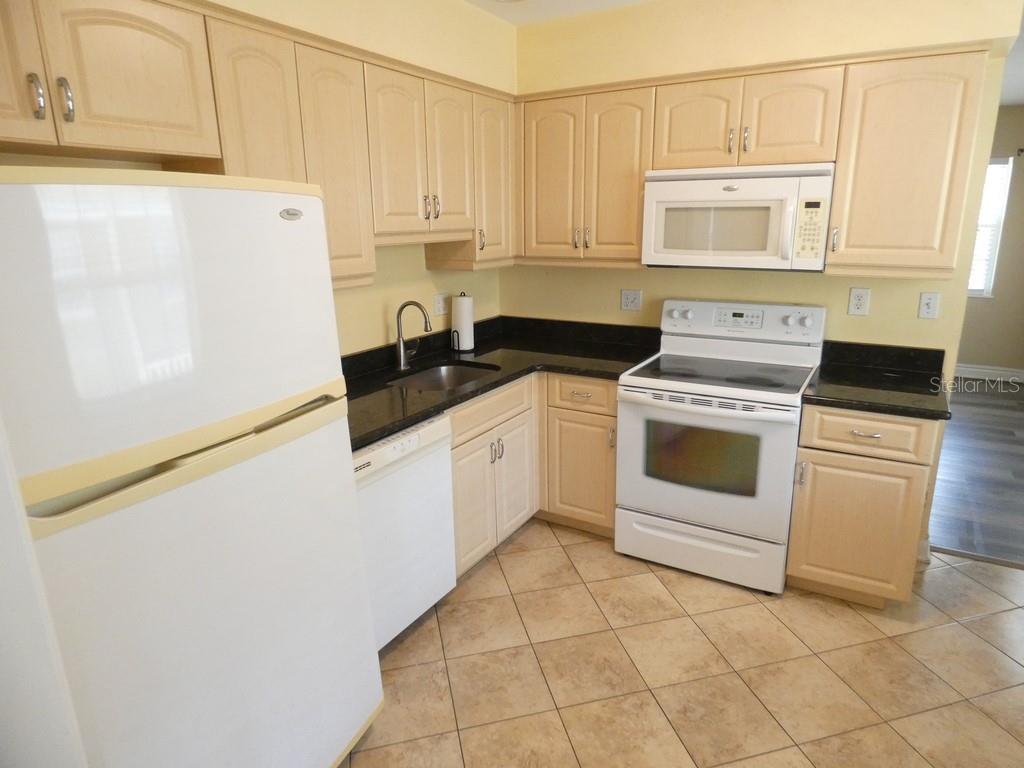 A kitchen features light wood cabinets, black countertops, white appliances, and beige tile flooring — 5220 11TH AVENUE N, ST PETERSBURG, FL