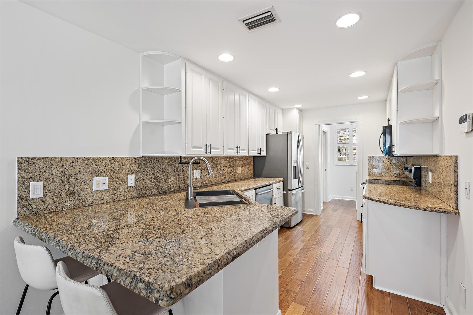 A kitchen features white cabinets, granite countertops, stainless steel appliances, and wood-look flooring — 442 Capistrano Drive, Palm Beach Gardens FL 33410, PALM BEACH GARDENS, FL