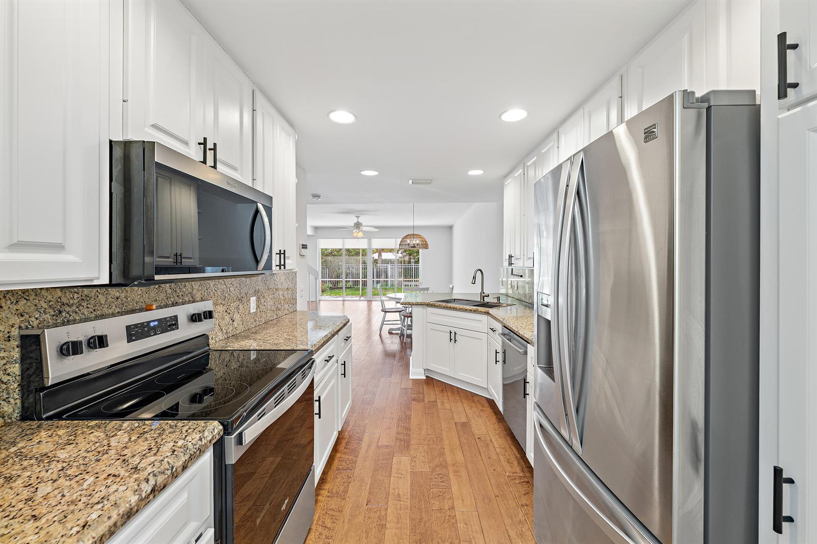 A kitchen with white cabinets, granite countertops, stainless steel appliances, and hardwood flooring — 442 Capistrano Drive, Palm Beach Gardens FL 33410, PALM BEACH GARDENS, FL