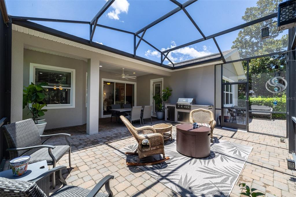 A screened-in patio features a brick paver floor, outdoor furniture, and a built-in grill station — 1130 GARDENSHIRE LANE, DELAND, FL