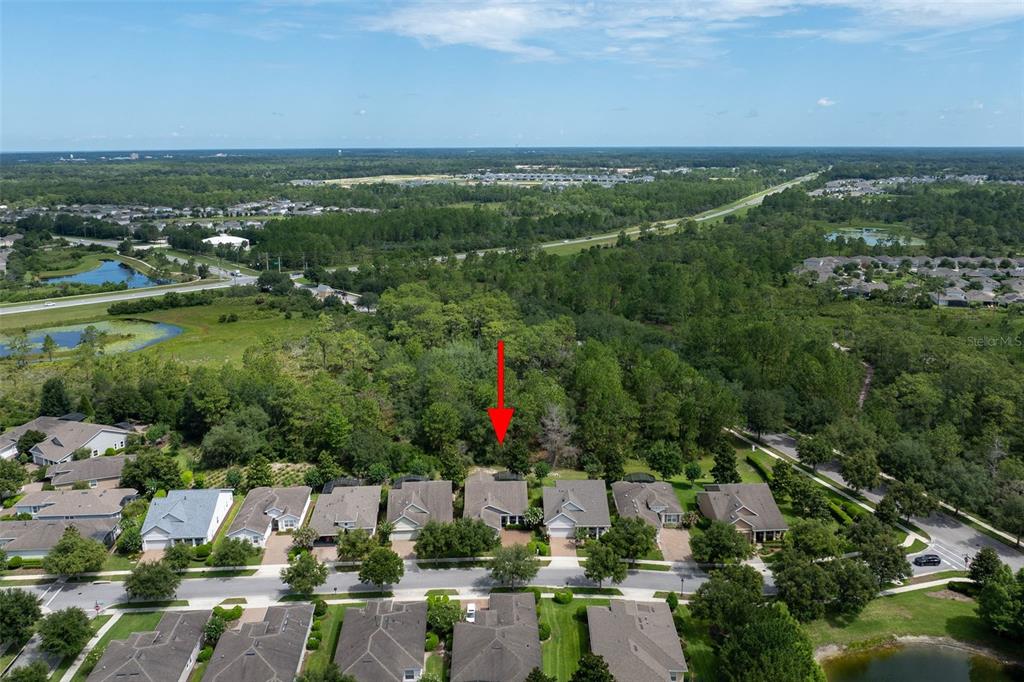 An aerial view shows a suburban neighborhood with a red arrow pointing to a house — 1130 GARDENSHIRE LANE, DELAND, FL