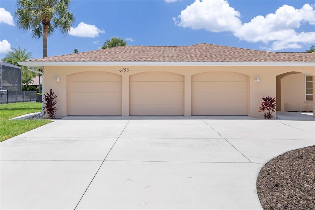 A three-car garage with beige doors is attached to a house with a tan exterior — 6755 AVENUE B, SARASOTA, FL