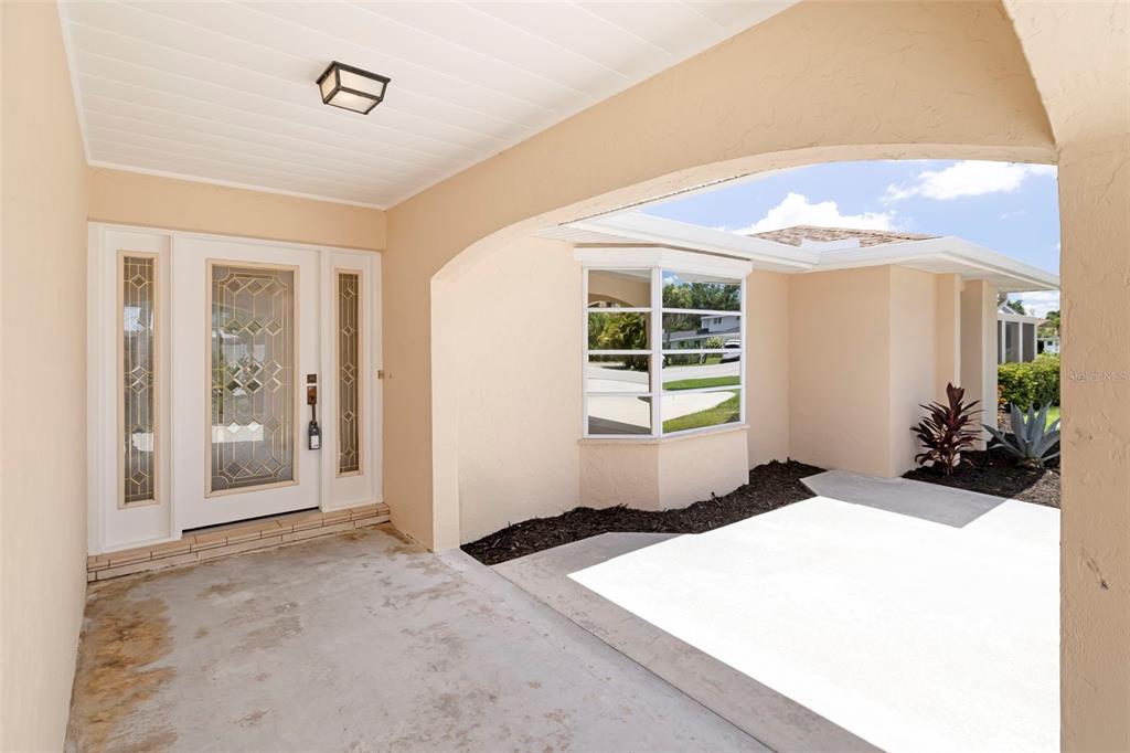 A covered concrete entryway features a white front door with decorative glass and a bay window — 6755 AVENUE B, SARASOTA, FL