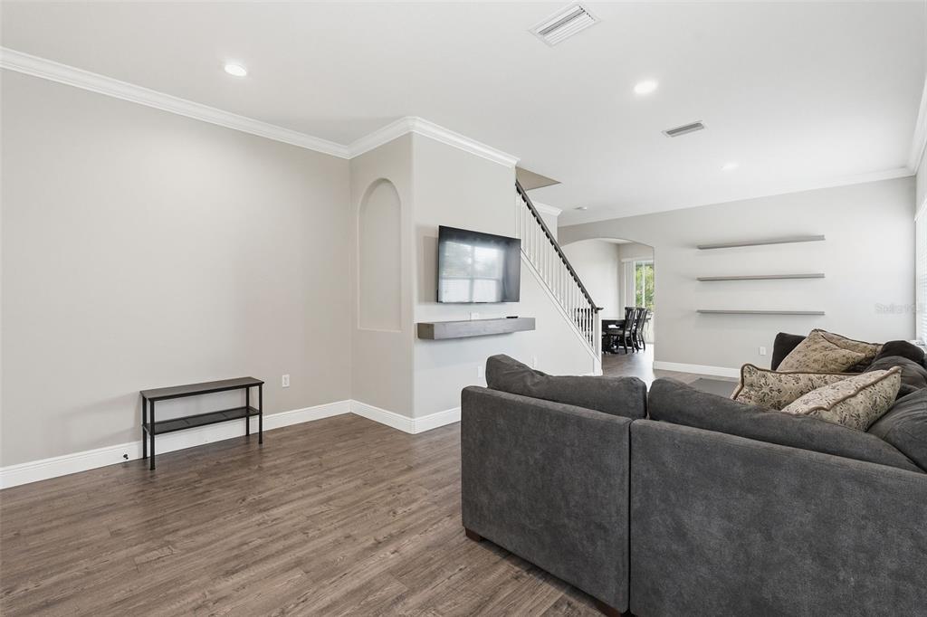 A living room with wood-look flooring, a gray sectional sofa, and a wall-mounted television — 8836 CAMERON CREST DRIVE, TAMPA, FL