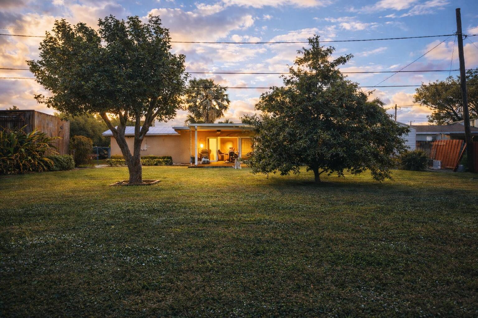 A backyard view of a one-story house with two large trees and a lit patio — 3526 Elizabeth Road, FL 33461, FL