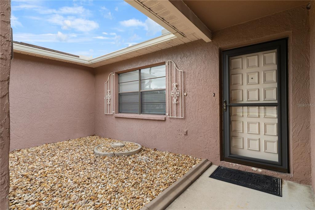 A tan stucco exterior wall features a window with decorative shutters and a front door — 2354 DELTONA BOULEVARD, SPRING HILL, FL