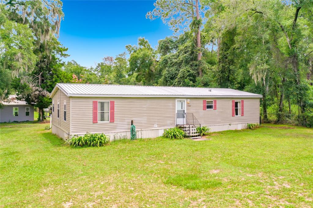 A single-story manufactured home with beige siding and red shutters sits on a grassy lot — 1021 NW 111TH COURT, OCALA, FL
