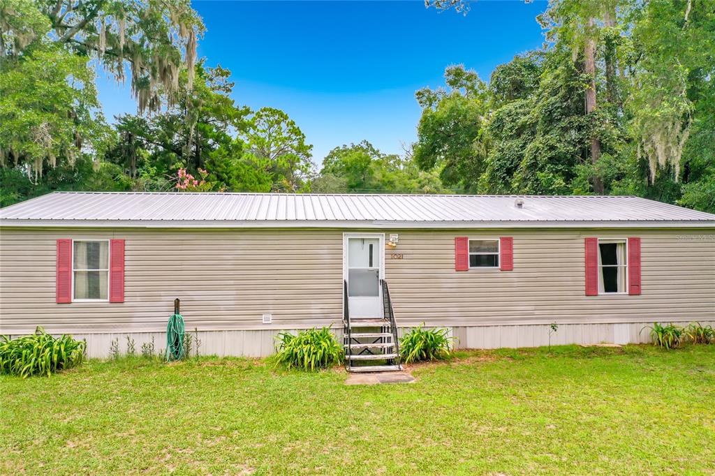 A single-story manufactured home with light siding, a metal roof, and red window shutters — 1021 NW 111TH COURT, OCALA, FL