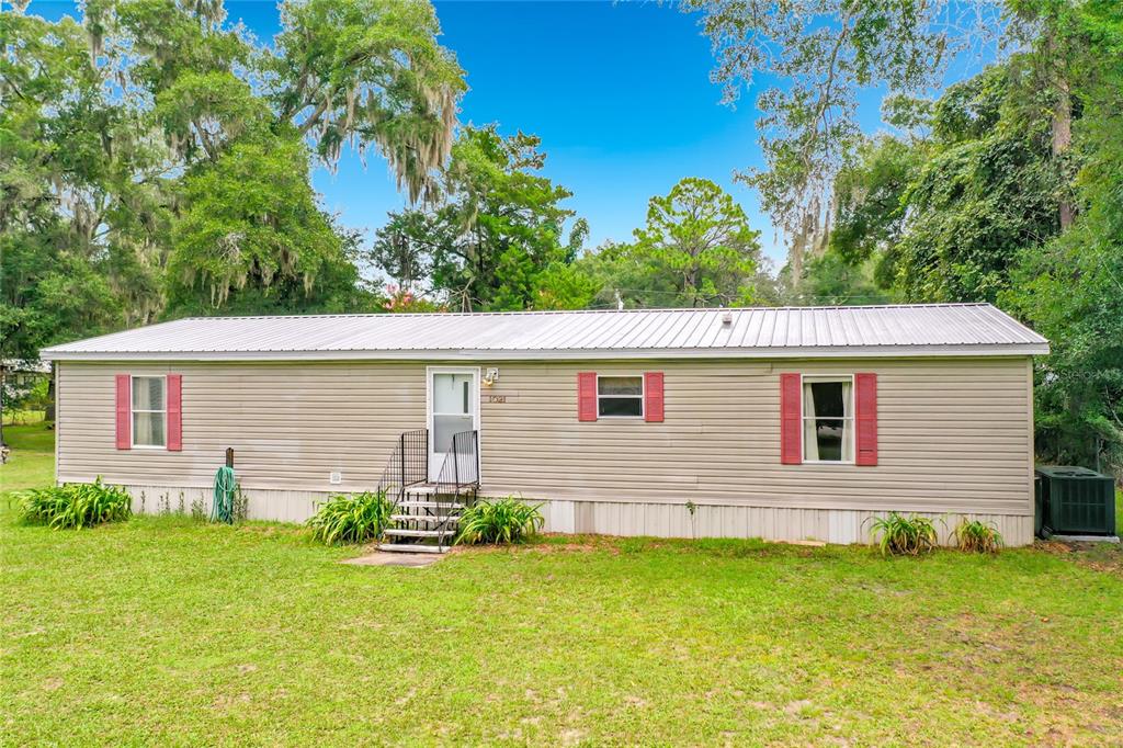 A single-story manufactured home with light siding, red shutters, and a metal roof — 1021 NW 111TH COURT, OCALA, FL