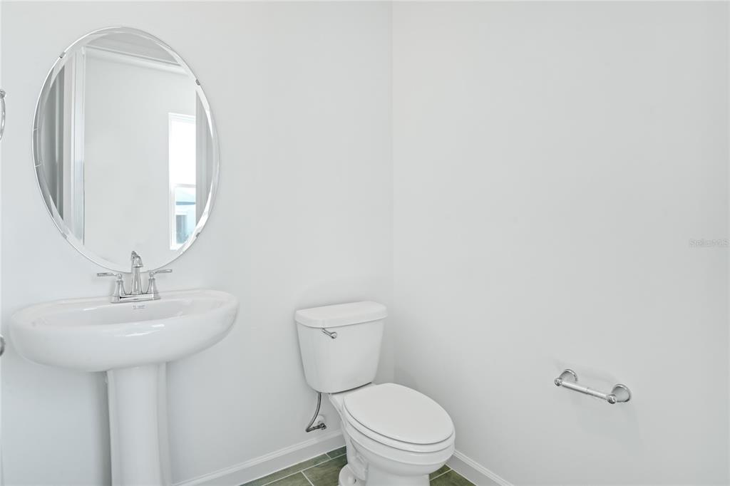 A half bathroom features a pedestal sink, an oval mirror, and a white toilet — 5228 BEE BALM STREET, LAKE HAMILTON, FL