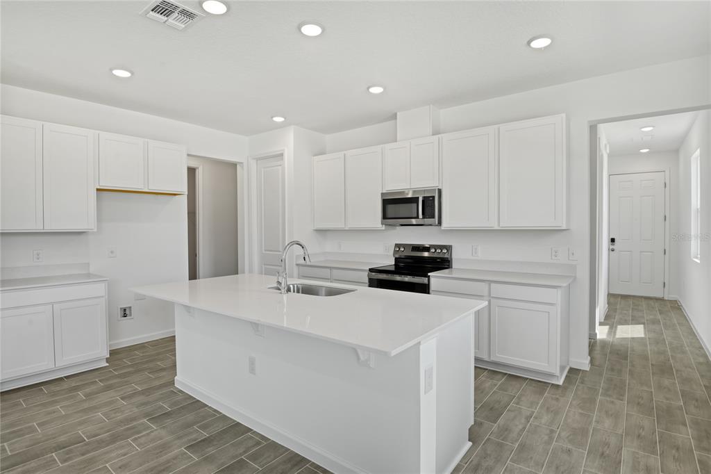 A modern kitchen features white cabinets, a large central island, and light wood-look tile flooring — 5228 BEE BALM STREET, LAKE HAMILTON, FL