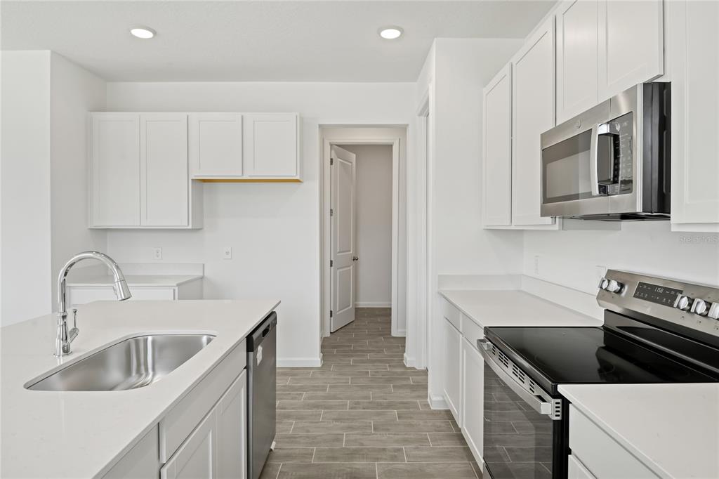 A modern kitchen features white cabinets, stainless steel appliances, a center island, and tile flooring — 5228 BEE BALM STREET, LAKE HAMILTON, FL