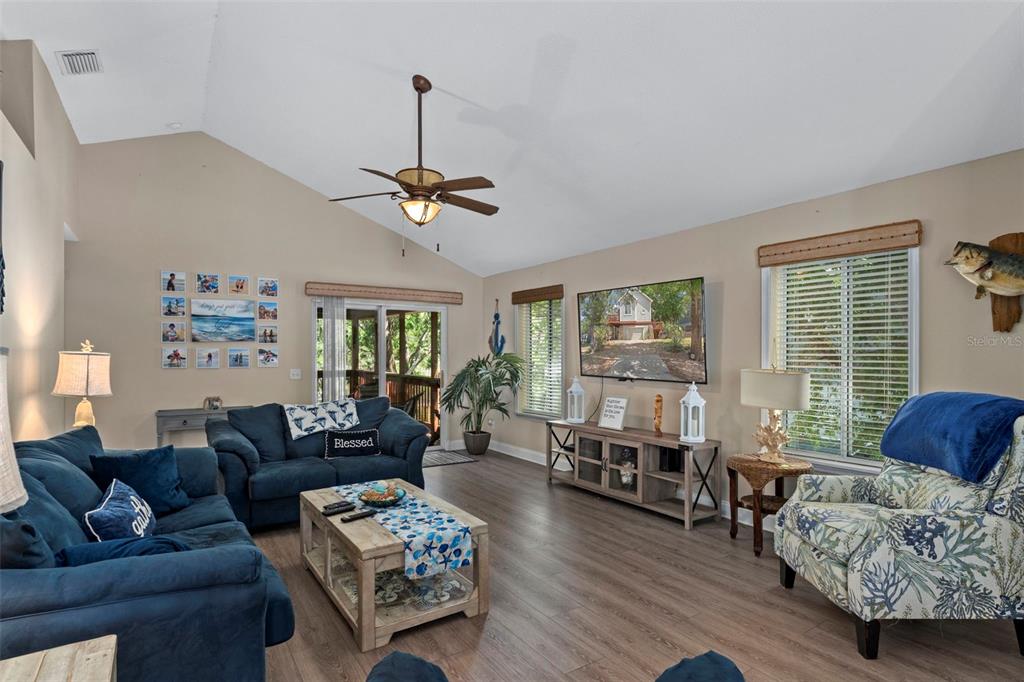 A living room with vaulted ceilings, blue furniture, a television, and wood-look flooring — 6779 S PINEBRANCH POINT, HOMOSASSA, FL