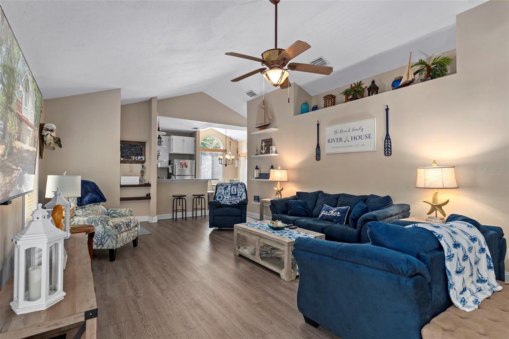 A living room with blue sofas, wood-look flooring, and nautical decor under a vaulted ceiling — 6779 S PINEBRANCH POINT, HOMOSASSA, FL